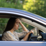 A woman sitting in a car with her hand on her forehead, looking stressed and overwhelmed.