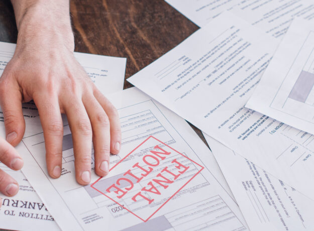 A person's hand resting on a stack of financial documents, with one paper prominently stamped “FINAL NOTICE” in red.