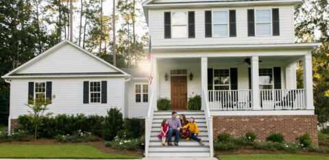 Family sitting on the front steps of a white suburban home with black shutters, enjoying time together outdoors.