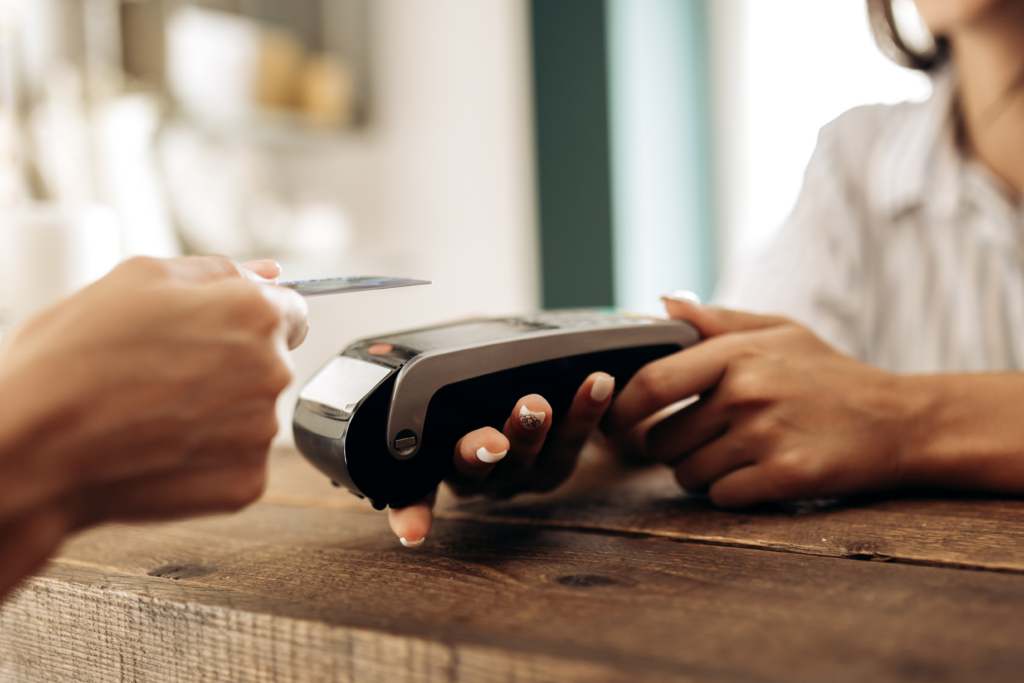 Close-up of a credit card being tapped on a card reader, with a cashier holding the payment terminal.