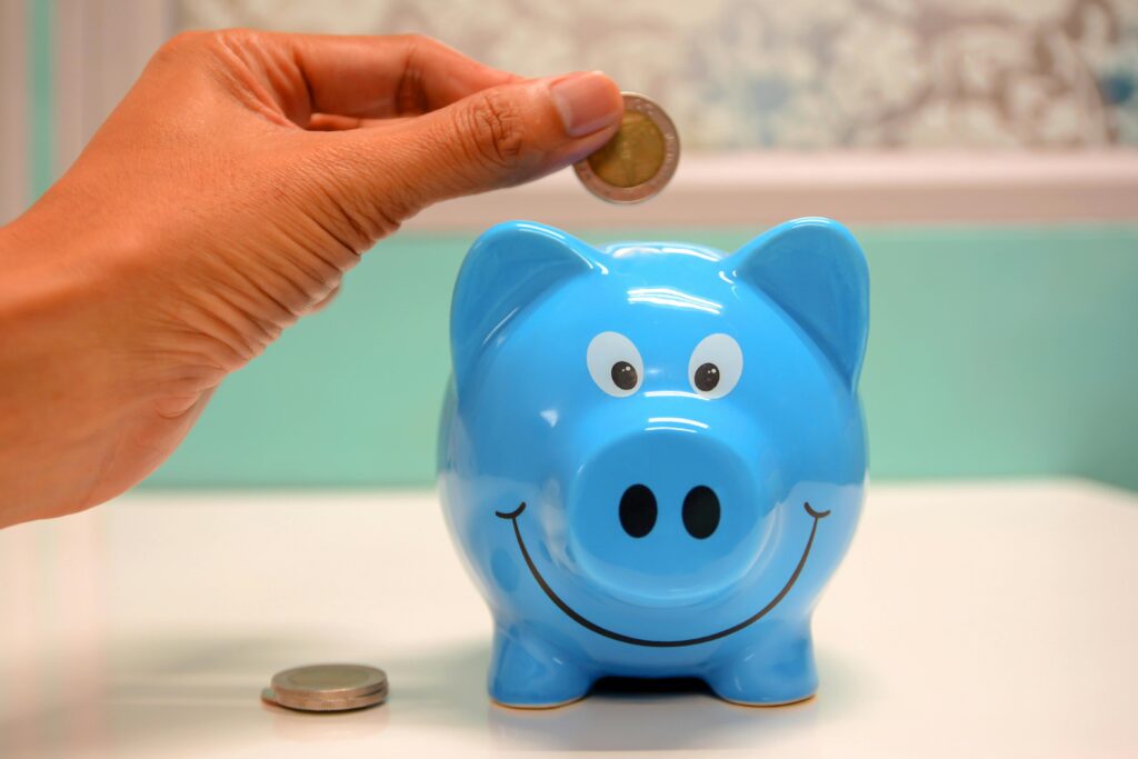 Smiling piggy bank with coins nearby and a hand about to add another coin.