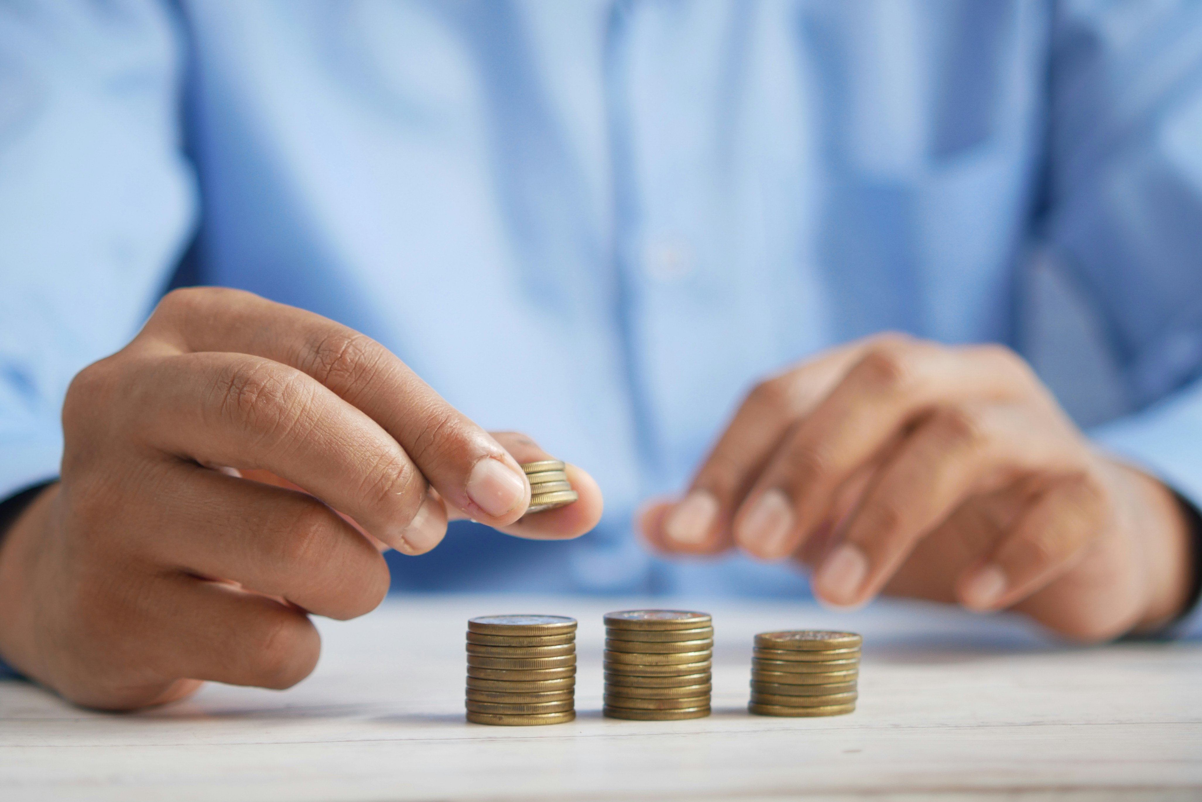 Person in a blue shirt stacking coins into neat piles on a white table, symbolizing budgeting or saving money.