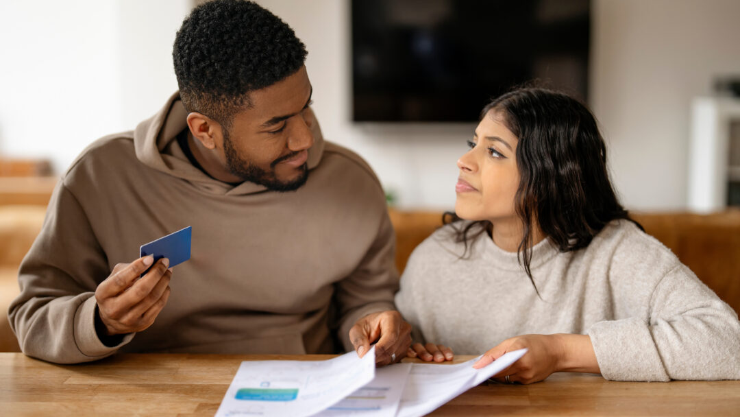 Young couple reviewing bills together at a table, holding a credit card