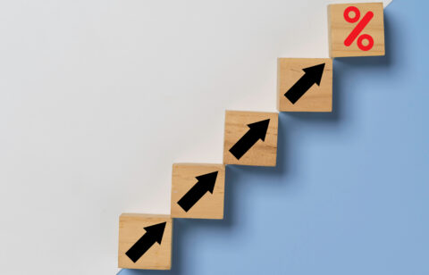 Conceptual staircase made of wooden cubes showing increasing arrows, ending in a percentage sign to represent growing interest rates or debt.