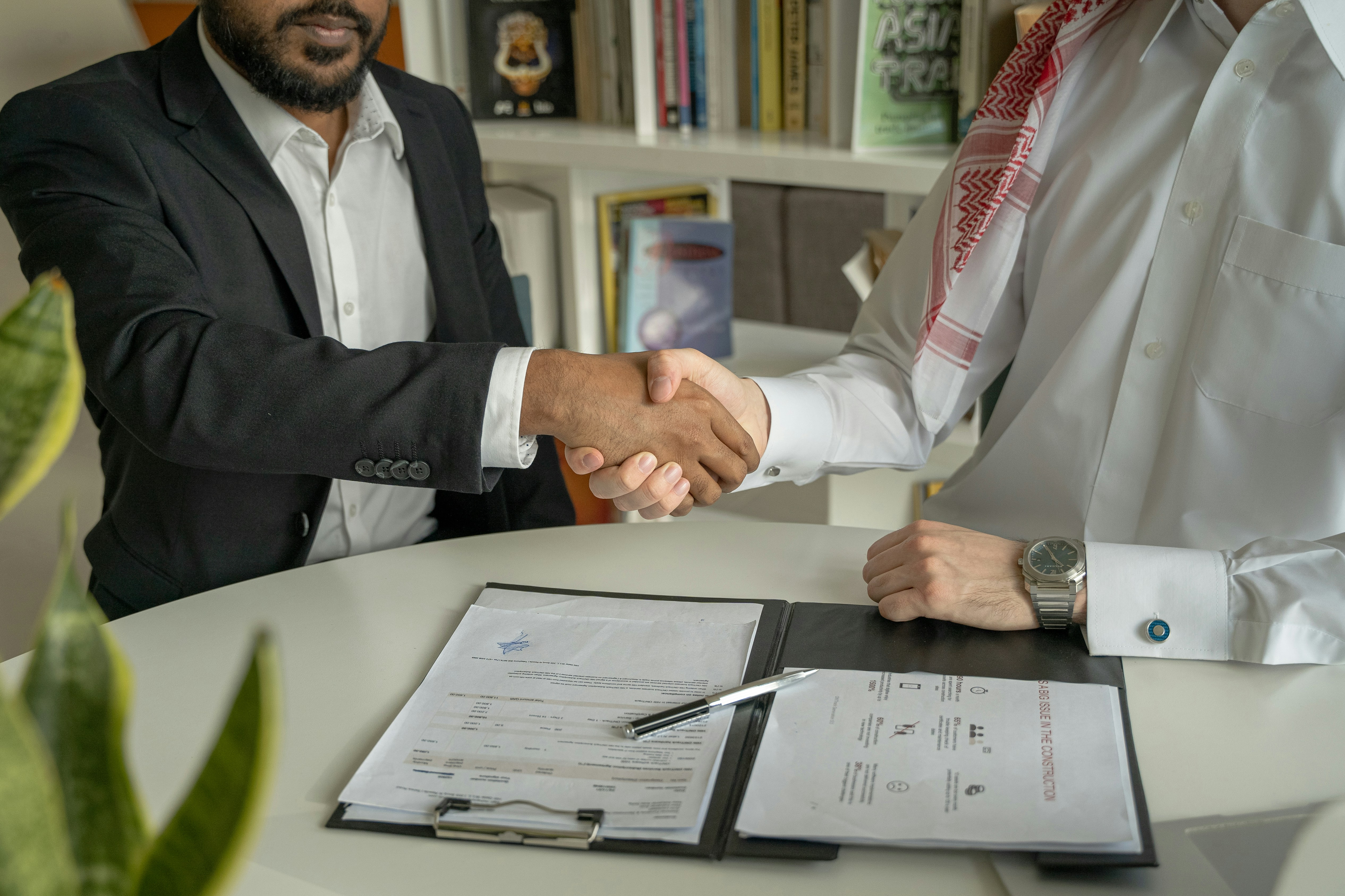 Two men shaking hands over a signed agreement at a desk