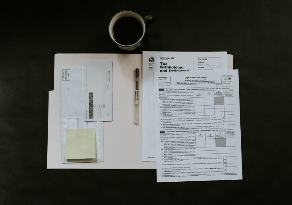 Tax forms and a pen organized on a folder, with a cup of coffee nearby.