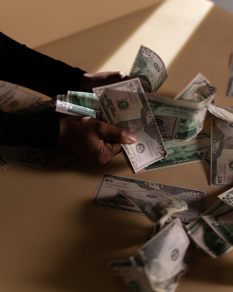 Person counting a large stack of U.S. dollar bills on a beige table under dramatic lighting.