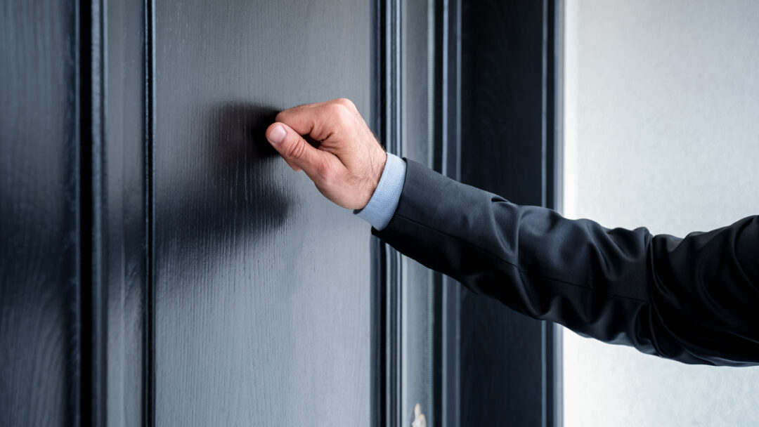 Close-up of a person's hand knocking on a residential door.