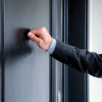 Close-up of a person's hand knocking on a residential door.