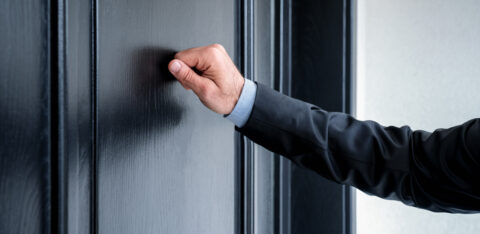 Close-up of a person's hand knocking on a residential door.