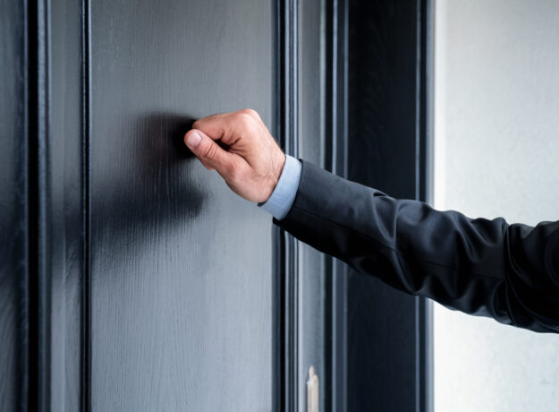 Close-up of a person's hand knocking on a residential door.