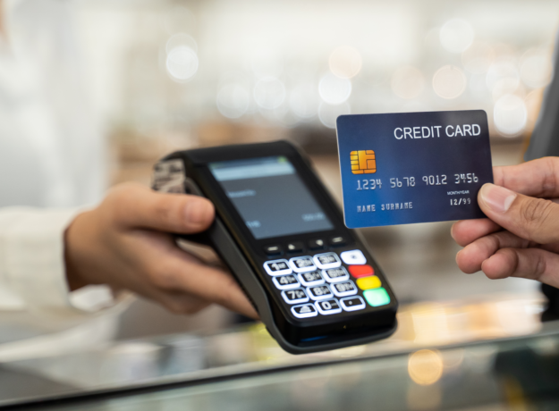 Person holding a credit card near a payment terminal for contactless transaction.