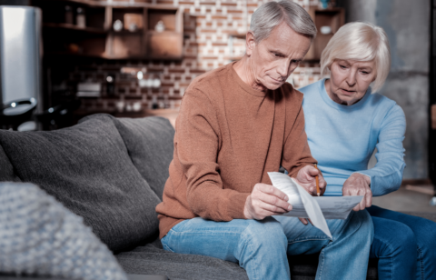 Senior couple sitting on a couch reviewing financial documents together.