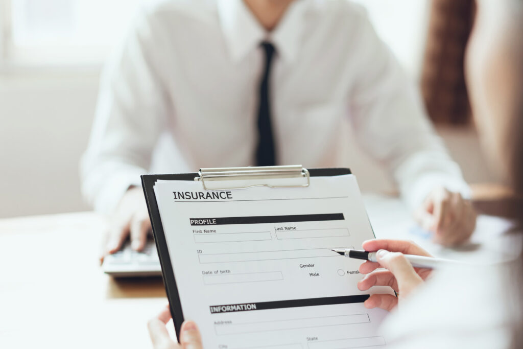 Close-up of a person filling out a health insurance form on a clipboard during a meeting.