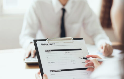 Close-up of a person filling out a health insurance form on a clipboard during a meeting.