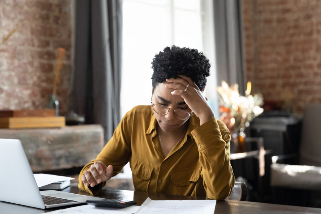 Person sitting at a desk looking stressed while reviewing documents with a laptop and calculator nearby