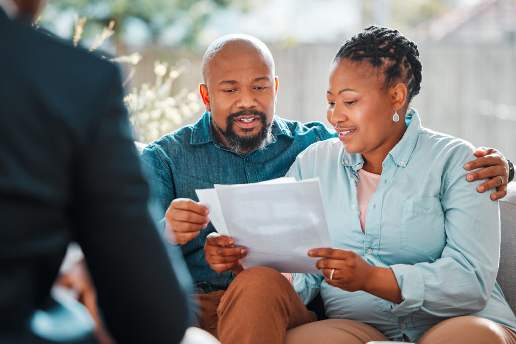 Smiling couple sitting close together while reviewing financial documents during a meeting with a professional.