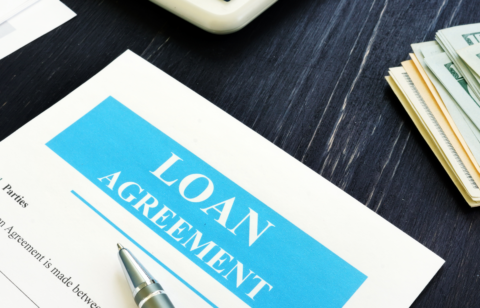 Close-up of a loan agreement document on a desk with a pen, cash, and calculator nearby.