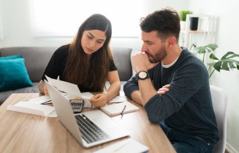 Couple sitting at a table reviewing financial documents with a laptop and calculator.