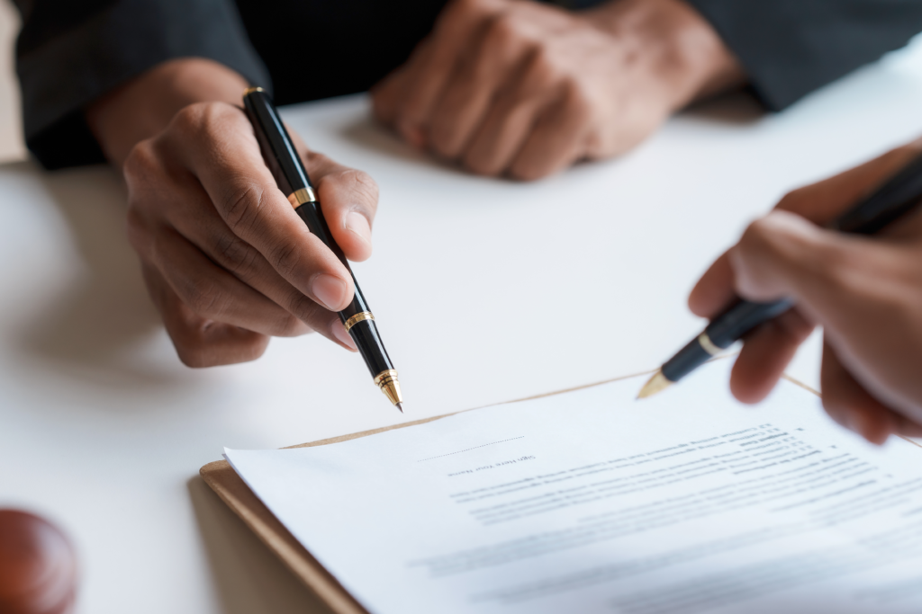 Two people holding pens while reviewing and signing a document on a clipboard.