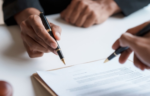 Two people holding pens while reviewing and signing a document on a clipboard.