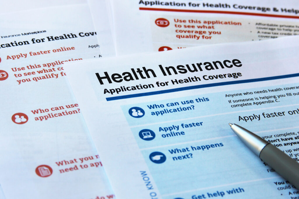 Close-up of health insurance application forms with a pen resting on one of the pages.