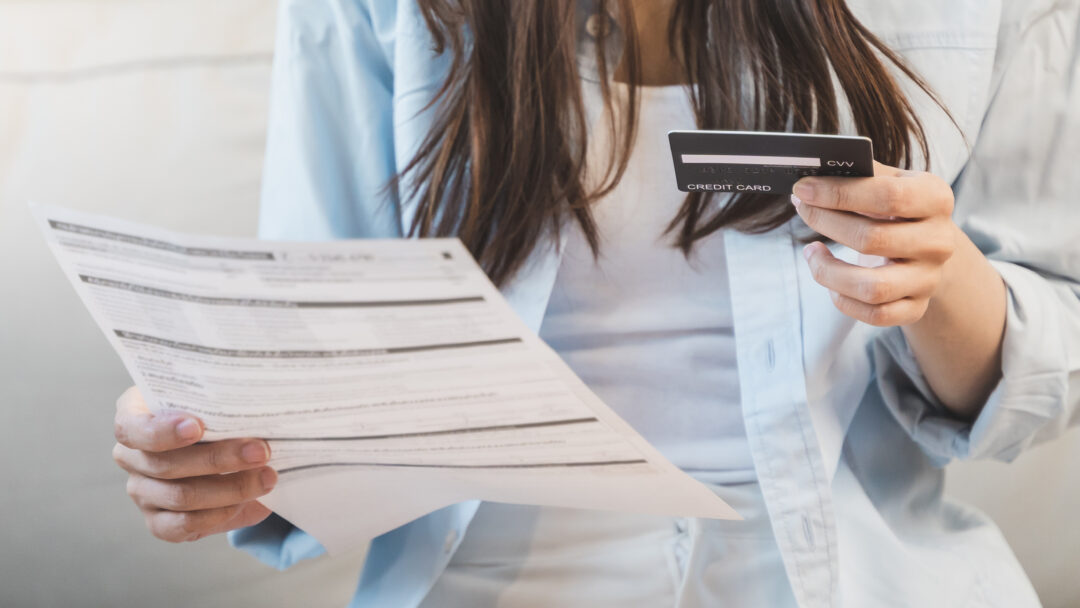 Woman reviewing a bill or financial statement while holding a credit card, seated indoors.