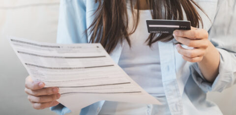 Woman reviewing a bill or financial statement while holding a credit card, seated indoors.
