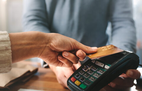 Close-up of a person making a contactless payment with a credit card at a card reader.