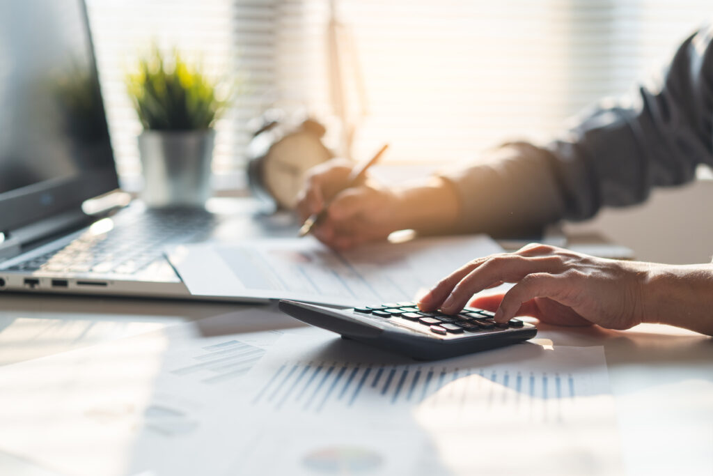 Person using a calculator and reviewing financial documents at a desk with a laptop.