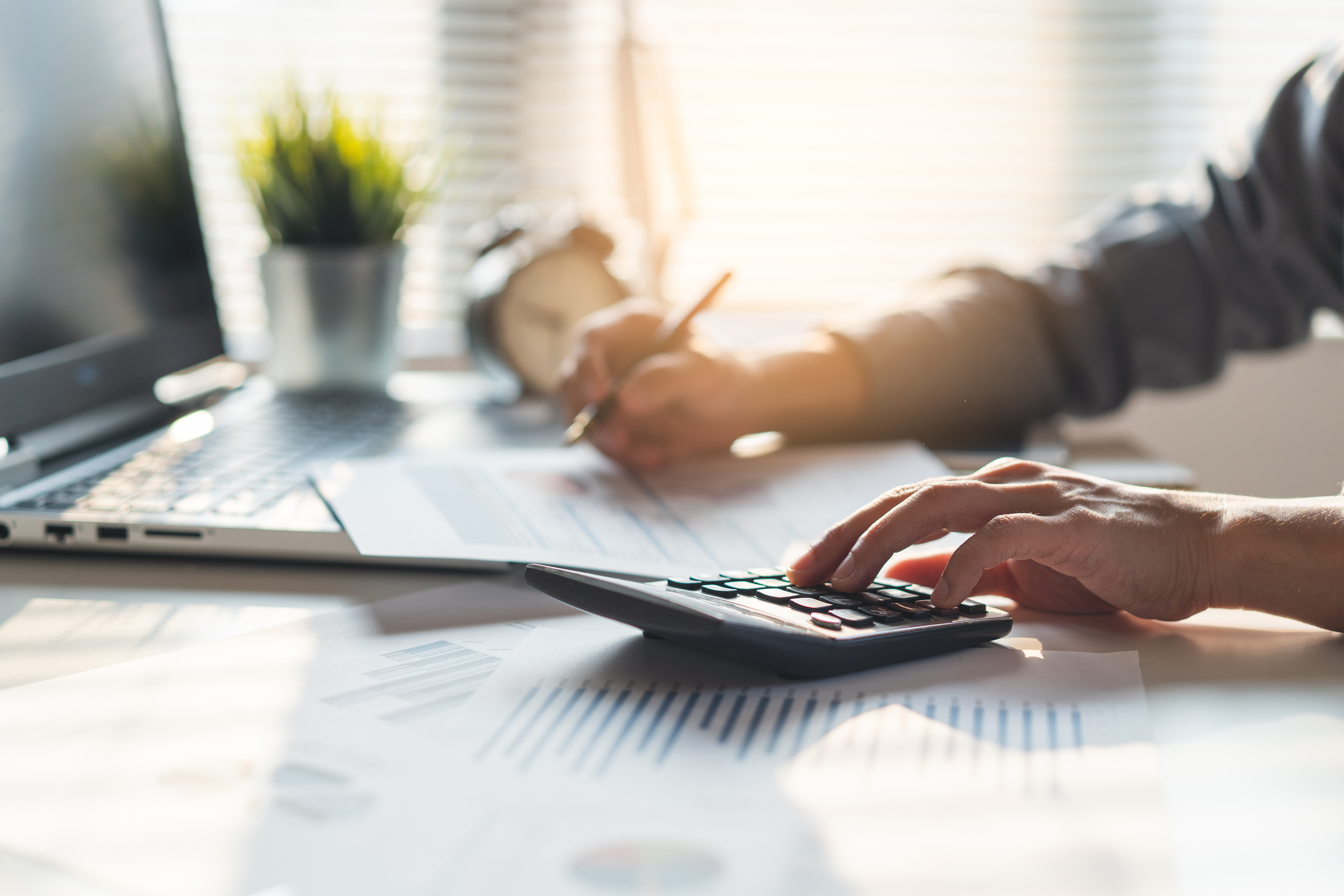 Person using a calculator and reviewing financial documents at a desk with a laptop.