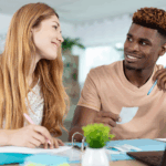 Smiling couple working together at a table with papers, receipts, and a laptop, possibly budgeting or reviewing finances.