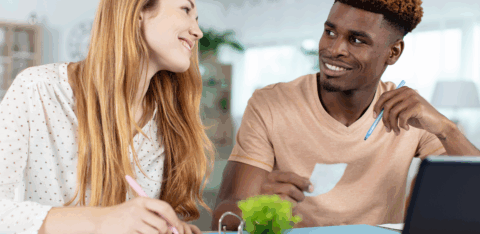 Smiling couple working together at a table with papers, receipts, and a laptop, possibly budgeting or reviewing finances.
