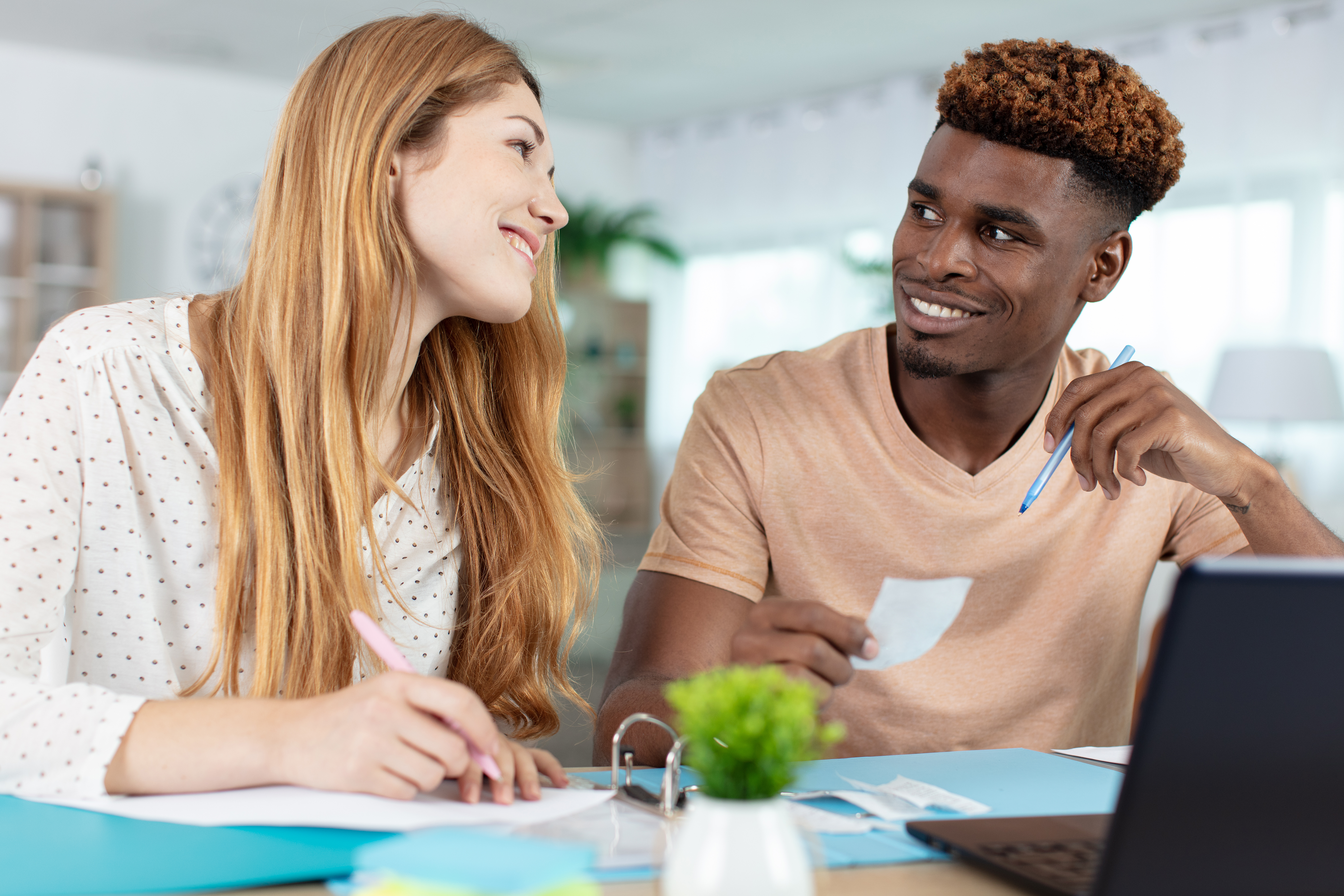 Smiling couple working together at a table with papers, receipts, and a laptop, possibly budgeting or reviewing finances.