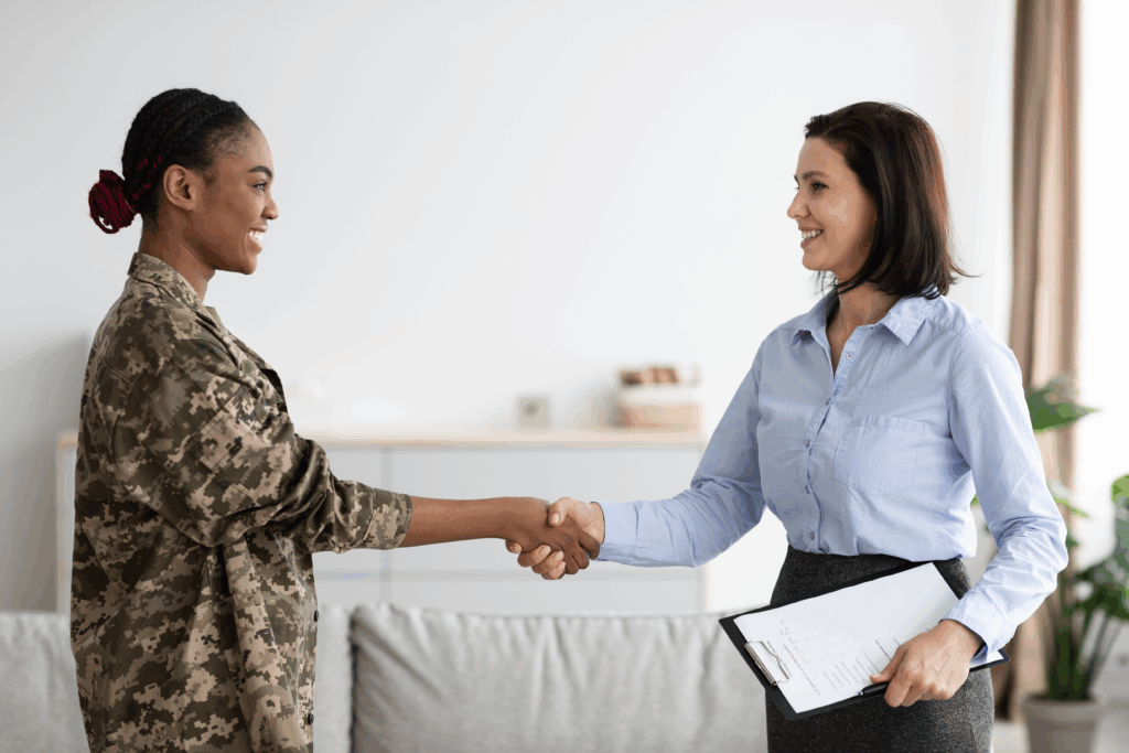 Smiling woman in military uniform shaking hands with a professional woman holding a clipboard.