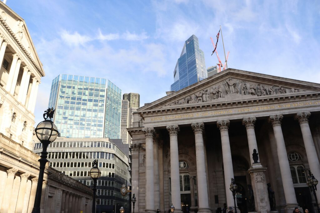 Front view of the Royal Exchange building in London, with modern skyscrapers in the background.