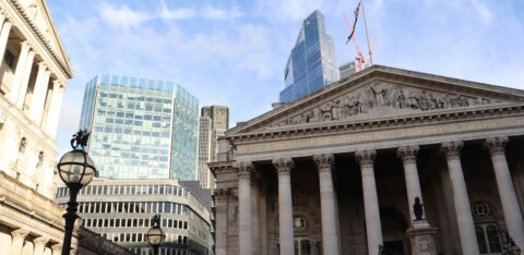 Front view of the Royal Exchange building in London, with modern skyscrapers in the background.