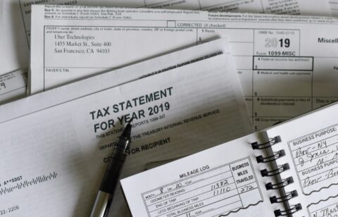 A collection of 2019 tax documents, including a 1099-MISC form from Uber Technologies, a tax statement envelope, a pen, and a mileage log notebook showing business miles traveled.
