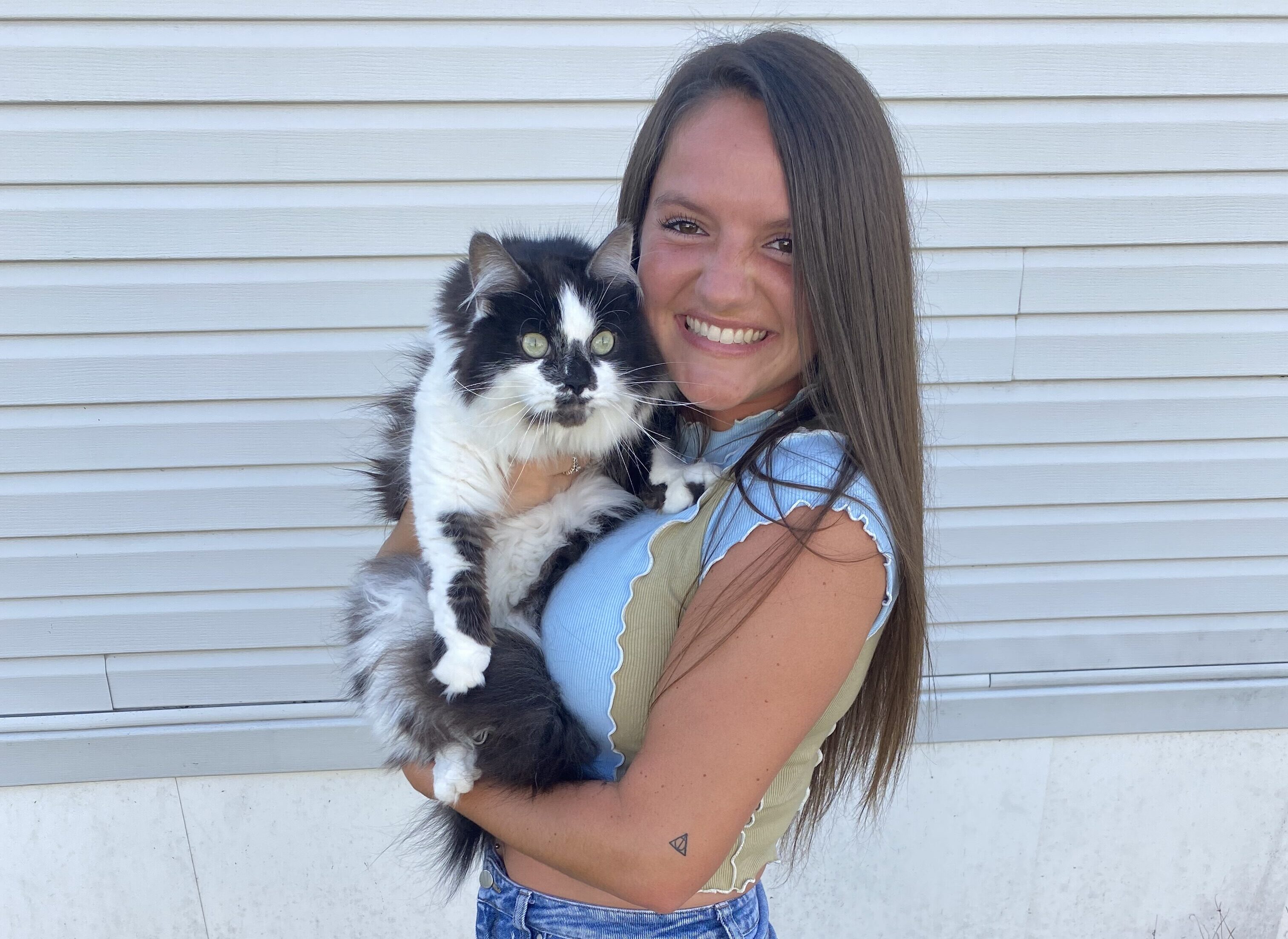 Young woman outdoors holding a fluffy cat, both looking at the camera