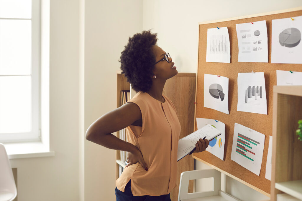 A woman holding a notebook studies charts and graphs pinned to a corkboard in an office.