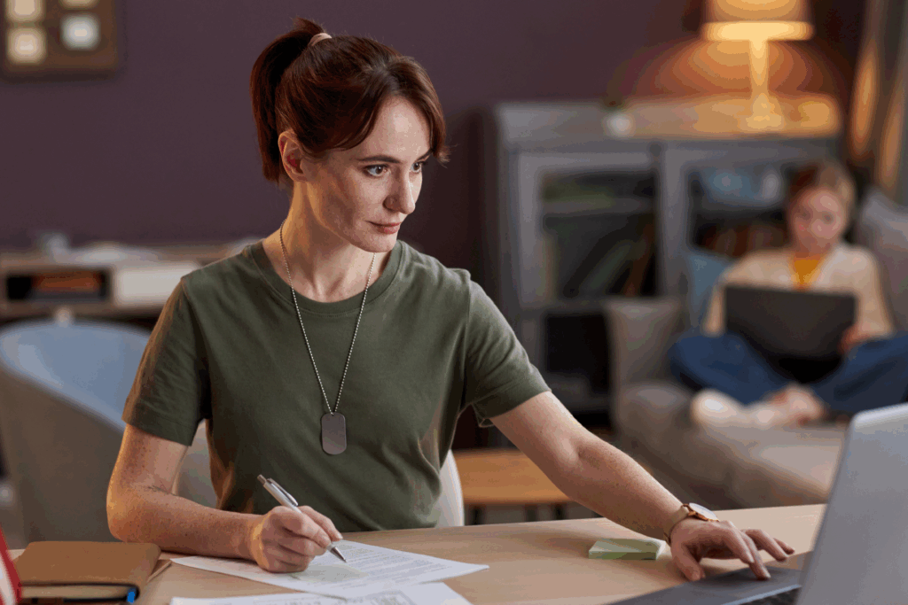 Veteran working on financial planning at a desk, with papers, a laptop, and another person in the background using a computer.