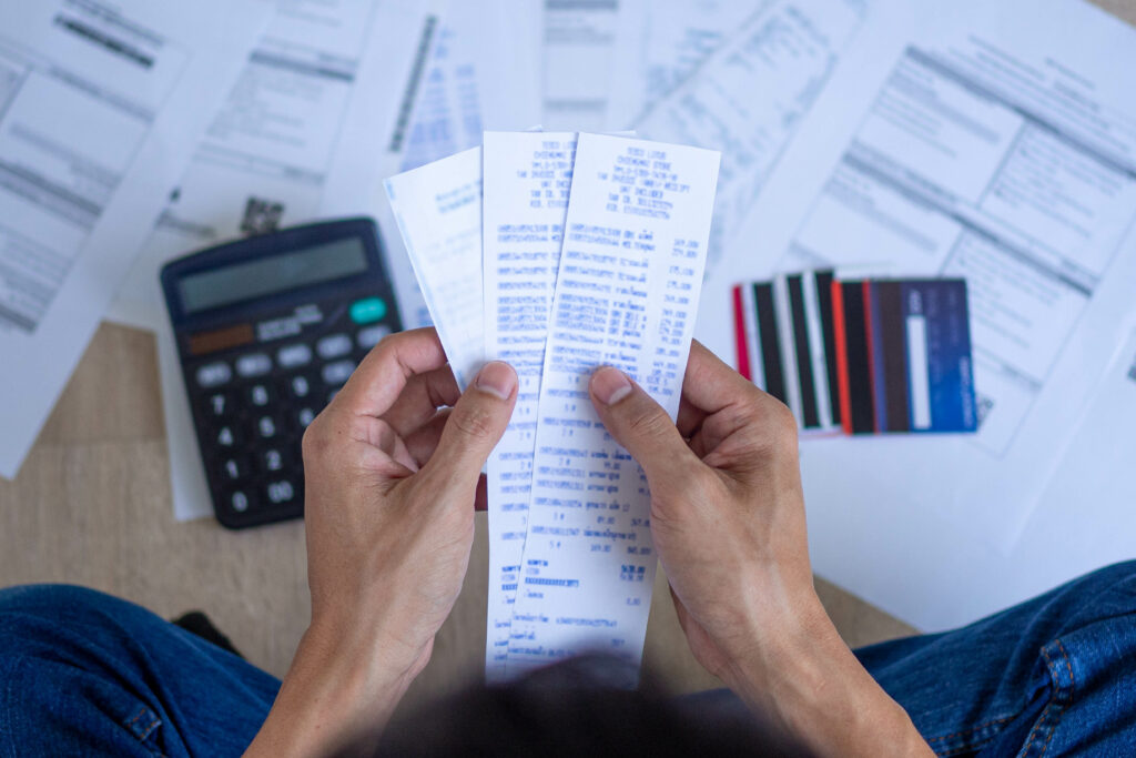 Person holding several receipts with a calculator, credit cards, and financial documents spread out on the floor.