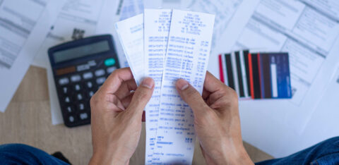 Person holding several receipts with a calculator, credit cards, and financial documents spread out on the floor.