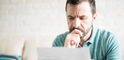 Man sitting on a couch, looking worried while reading a letter or bill.