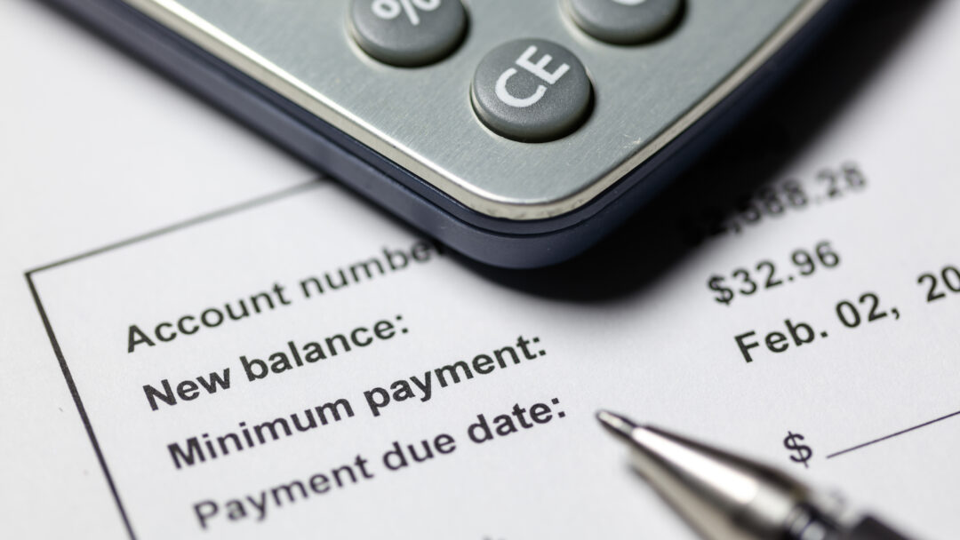 Close-up of a calculator on top of a billing statement showing account balance, minimum payment, and payment due date.