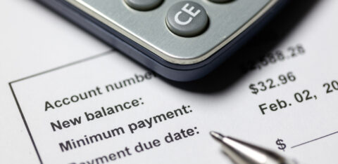 Close-up of a calculator on top of a billing statement showing account balance, minimum payment, and payment due date.