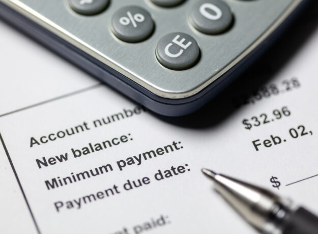 Close-up of a calculator on top of a billing statement showing account balance, minimum payment, and payment due date.