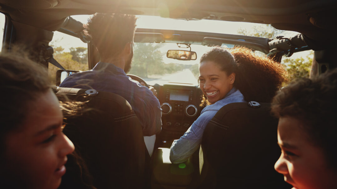 Family enjoying a road trip in a car with the mother smiling back at her children.