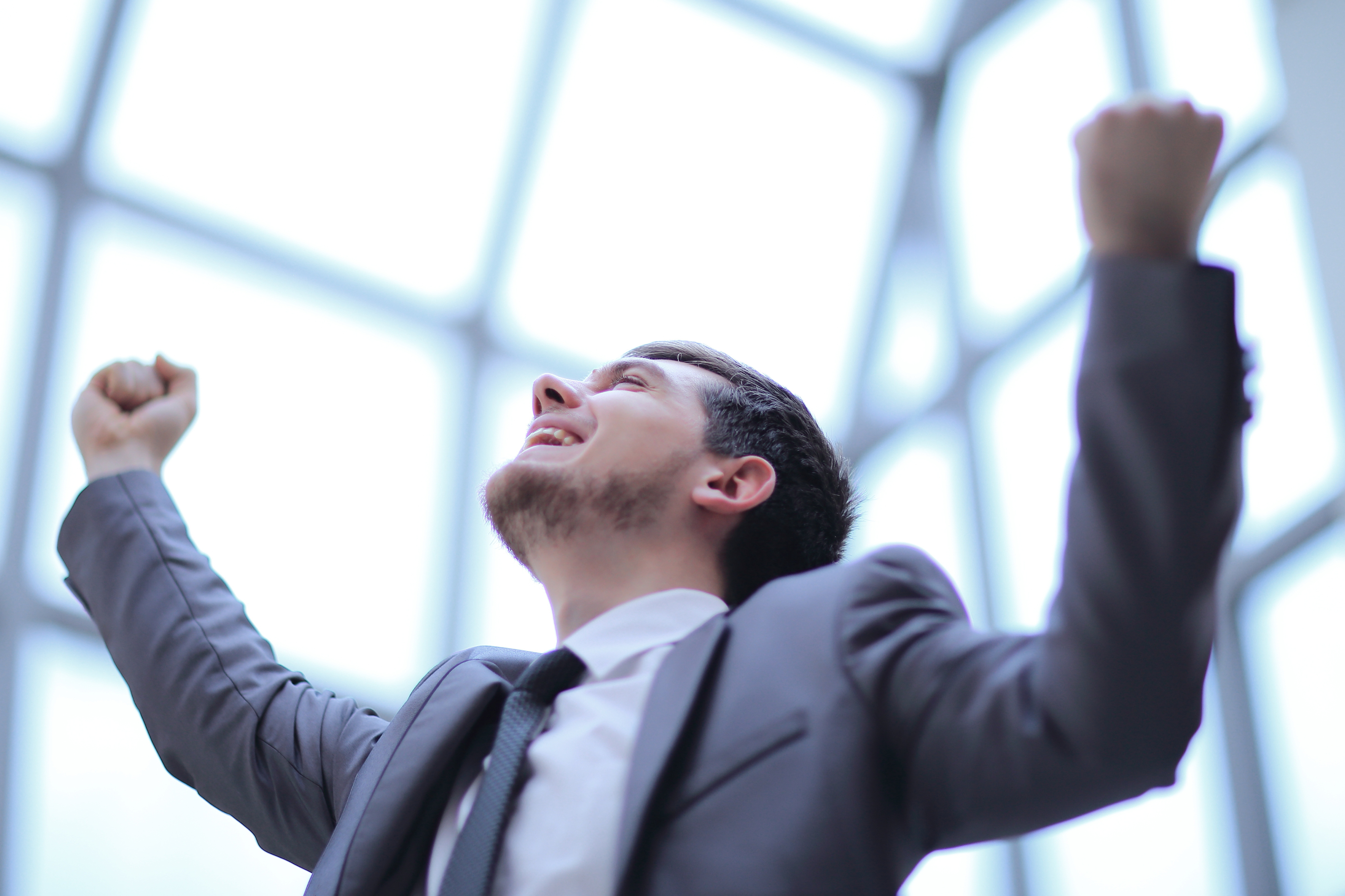 Young man in a suit cheering with arms lifted, expressing joy and success.