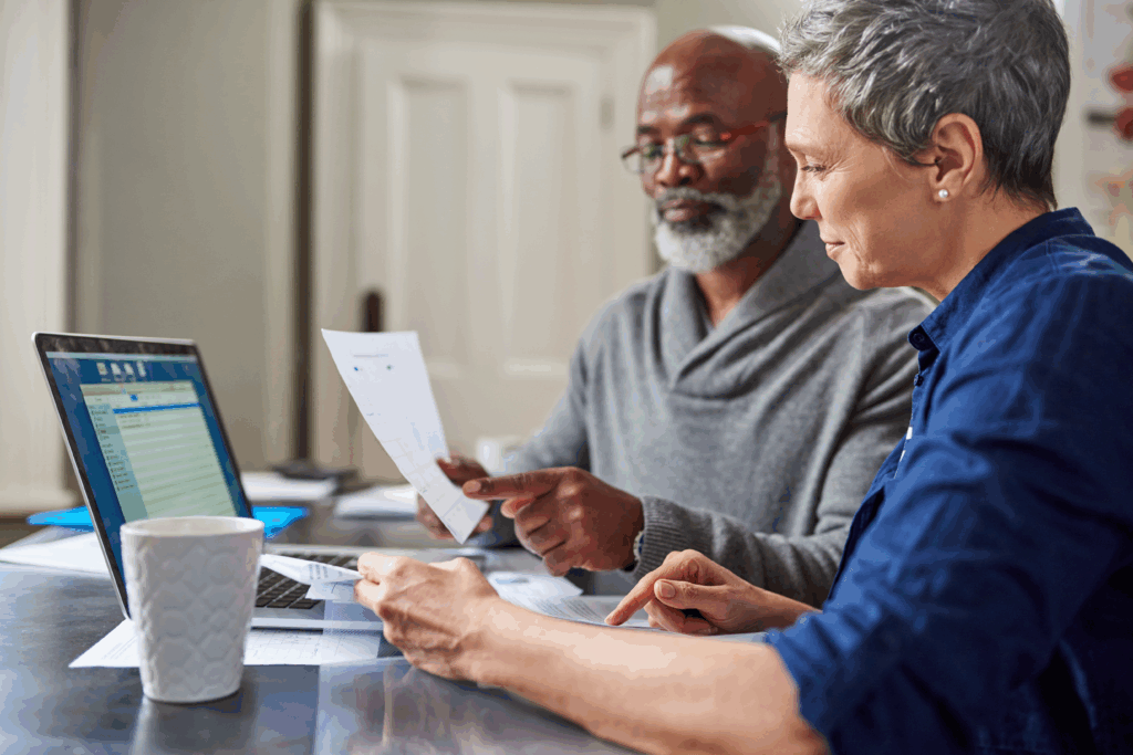 Older couple reviewing financial documents together at a table with a laptop.